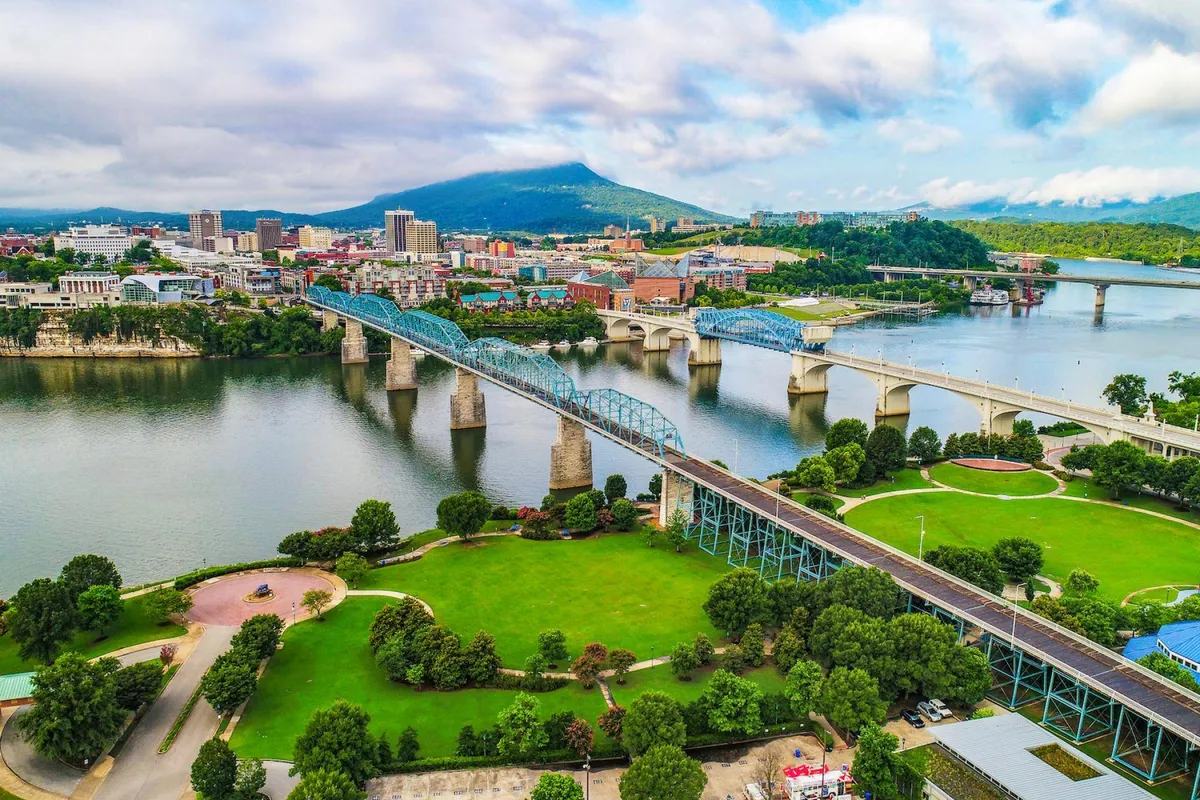 A beautiful exterior scene featuring a flowing river, an iconic bridge, the city skyline, and distant mountains. The area is lively yet inviting, suggesting abundant opportunities for walking, biking, picnicking, and exploring the urban-meets-nature environment.