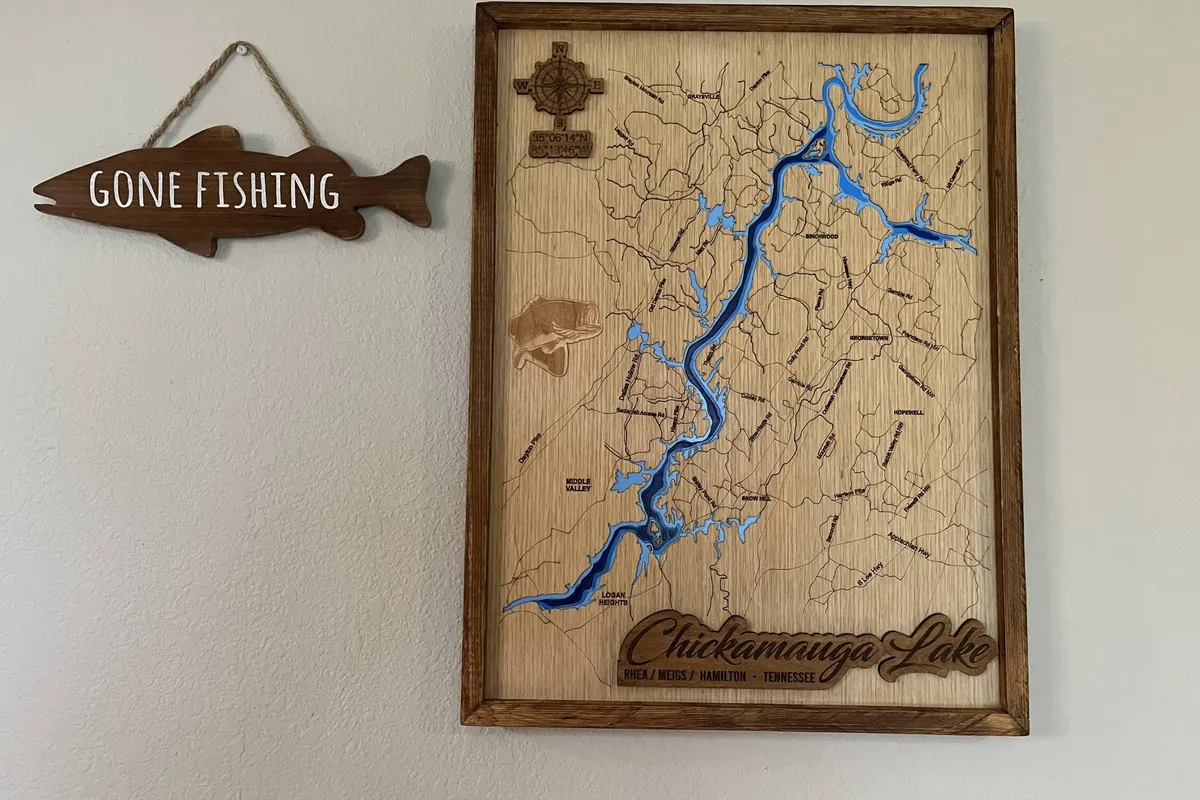 A cozy interior adorned with a wooden map of Chickamauga Lake and a 'Gone Fishing' sign, evoking a spirit of adventure and connection to local outdoor activities. The space feels casual and personal, hinting at the home's character and its ties to nearby exploration.