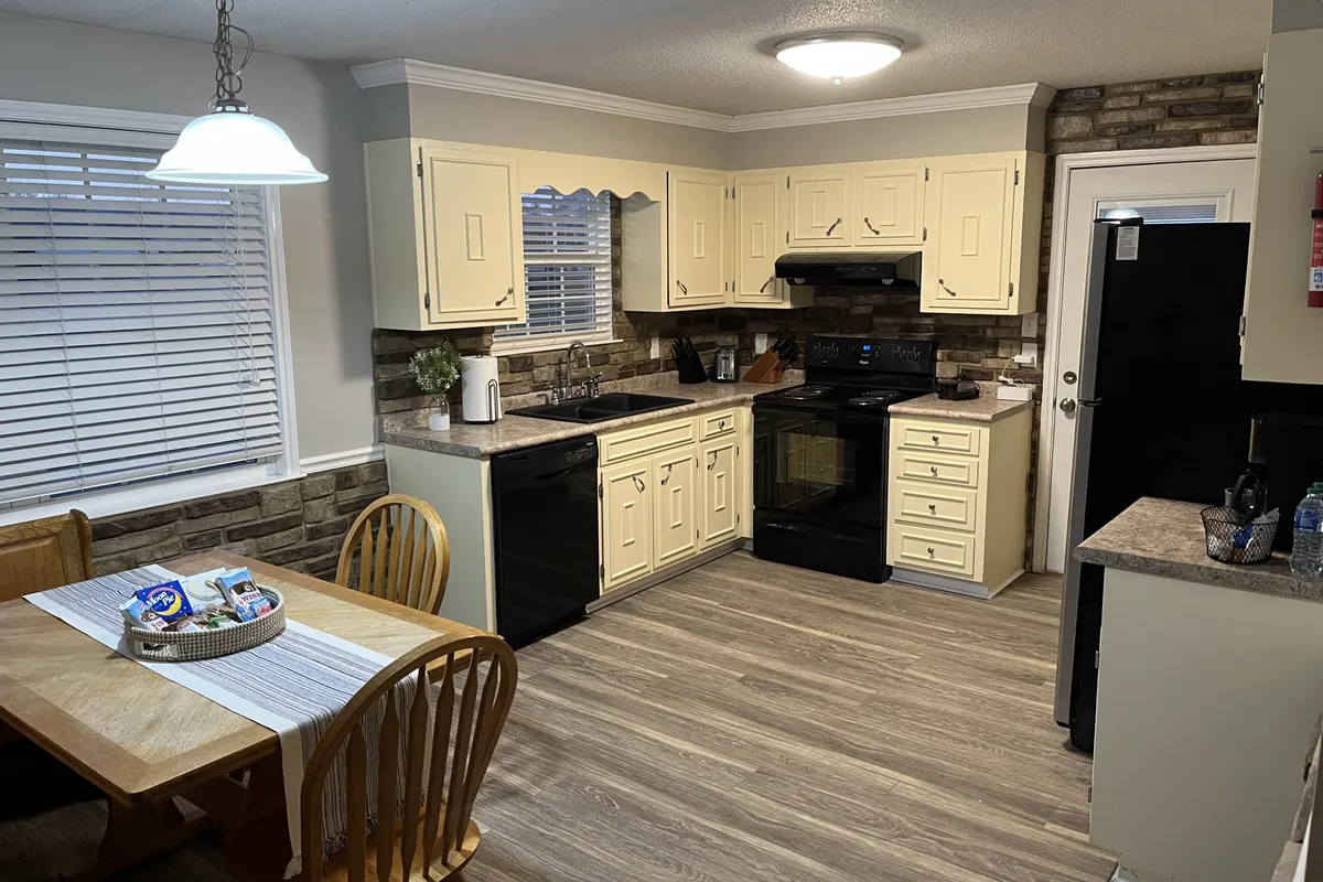 A warm, welcoming kitchen and dining area with a prominent kitchen island, a dining table for six, and modern black appliances. The island offers generous counter space, and the open setup encourages social cooking and gathering. Visible details include cookware and inviting décor, reinforcing the area as the home's central hub for shared meals and conversations.