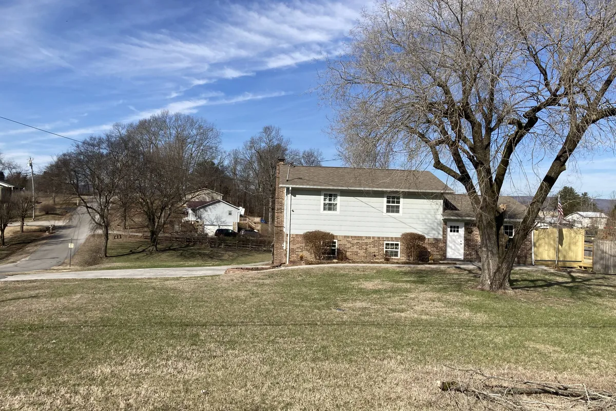 A wide view of the home showcasing a large tree, grassy front yard, and the house itself, offering ample space for children and pets to play. The setting is peaceful, perfect for family gatherings, games on the grass, or simply enjoying the outdoors.