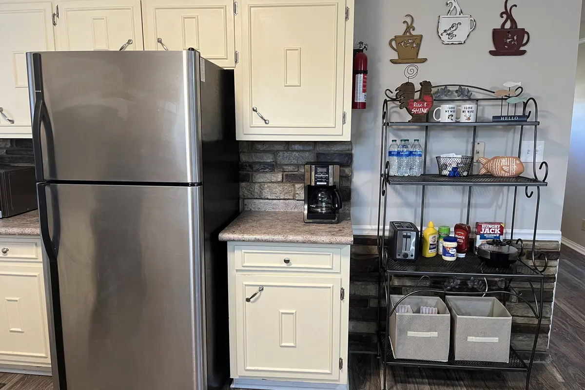 A cozy corner of the kitchen featuring a stainless steel refrigerator, coffee maker, and open shelving filled with decorative items. The image invites thoughts of meal preparation, morning coffee, and casual socializing, all in a comfortable and practical setting.